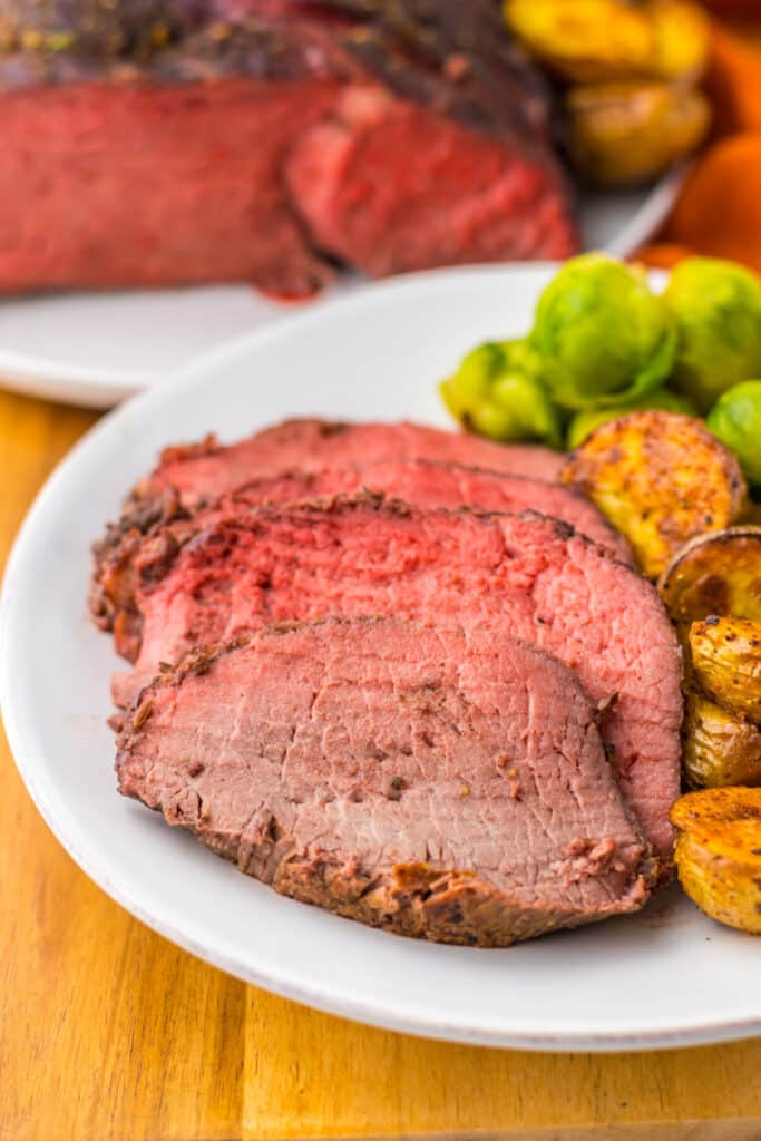Thick slices of prime rib roast with roasted potatoes on white plate