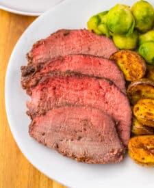 Thick slices of prime rib roast with roasted potatoes on white plate
