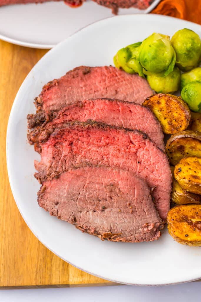 Thick slices of prime rib roast with roasted potatoes on white plate