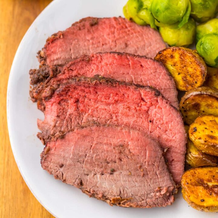 Thick slices of prime rib roast with roasted potatoes on white plate