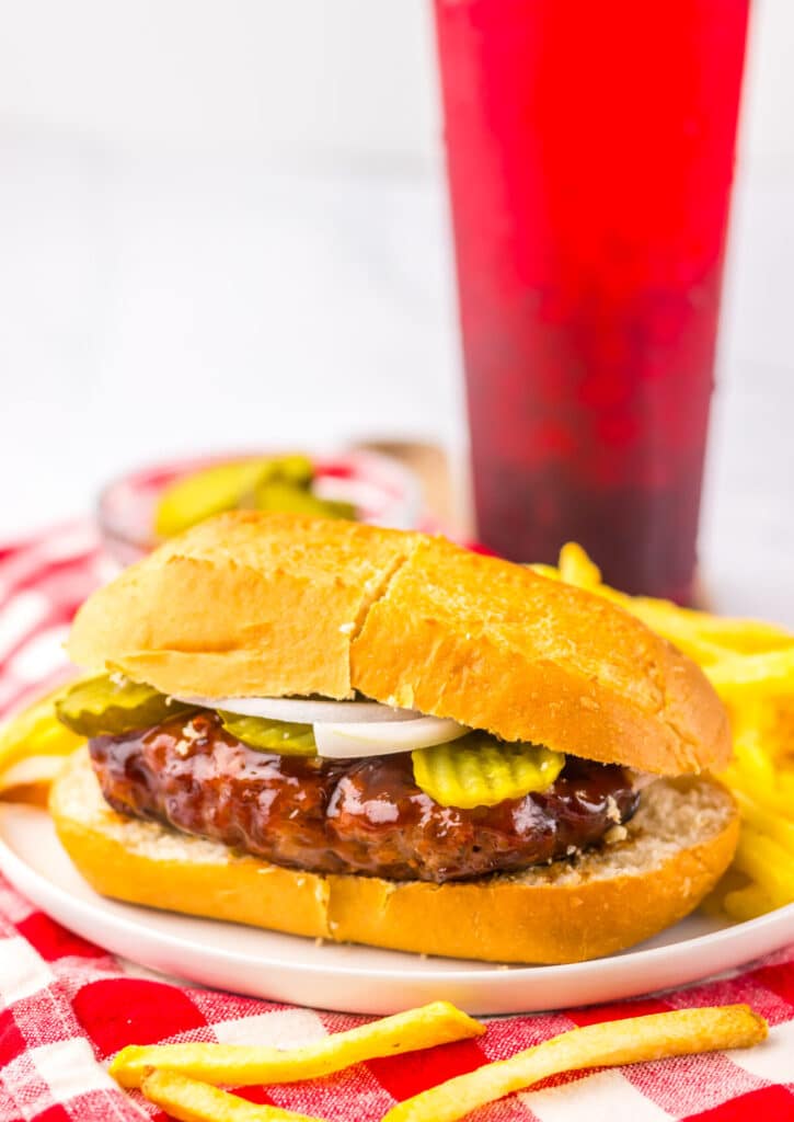 Close-up of a saucy McRib copycat sandwich with pickles and onions, served with fries on a red and white napkin.