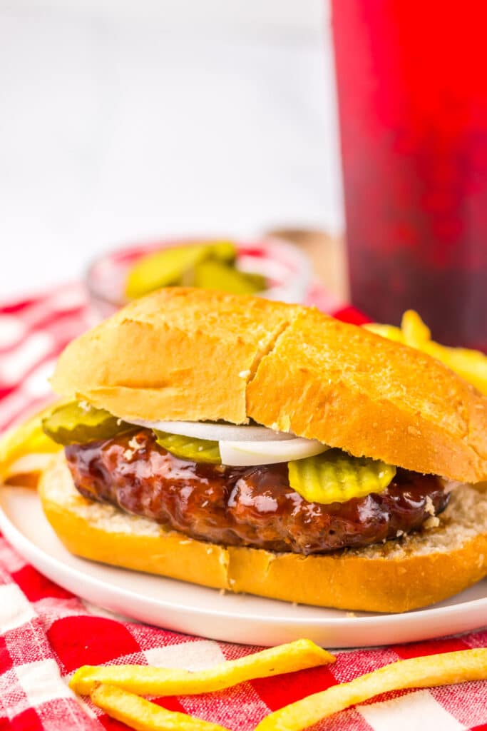 Juicy BBQ pork sandwich styled like the McRib, plated with crispy fries and a checkered red and white napkin.