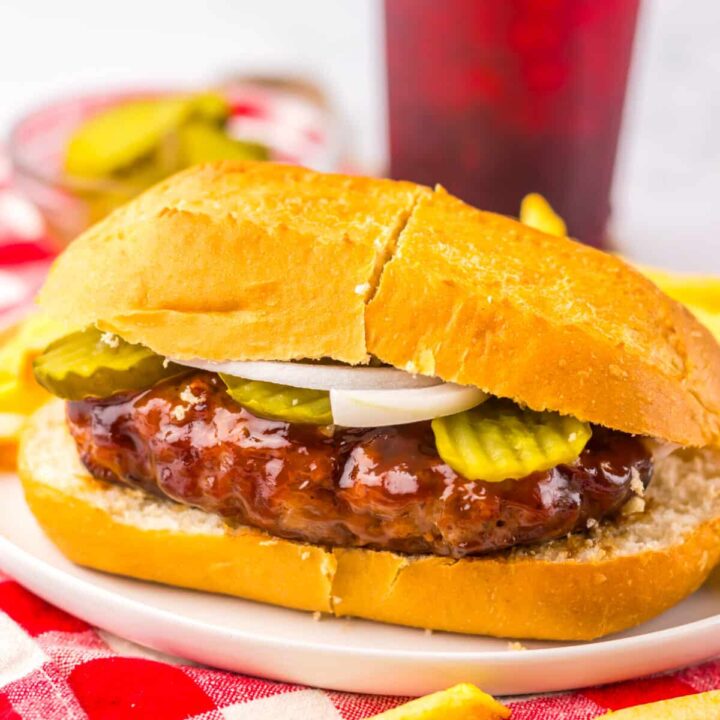 Copycat McRib sandwich topped with onions and pickles, served with fries on a rustic plate and red and white napkin.