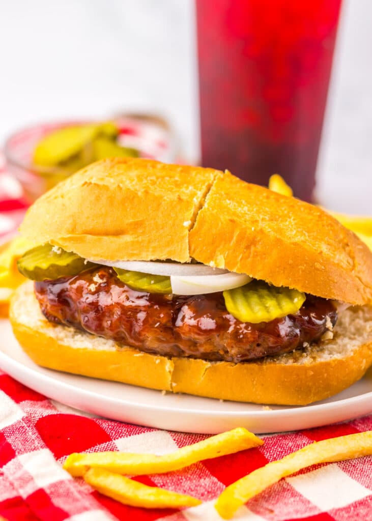 Copycat McRib sandwich topped with onions and pickles, served with fries on a rustic plate and red and white napkin.