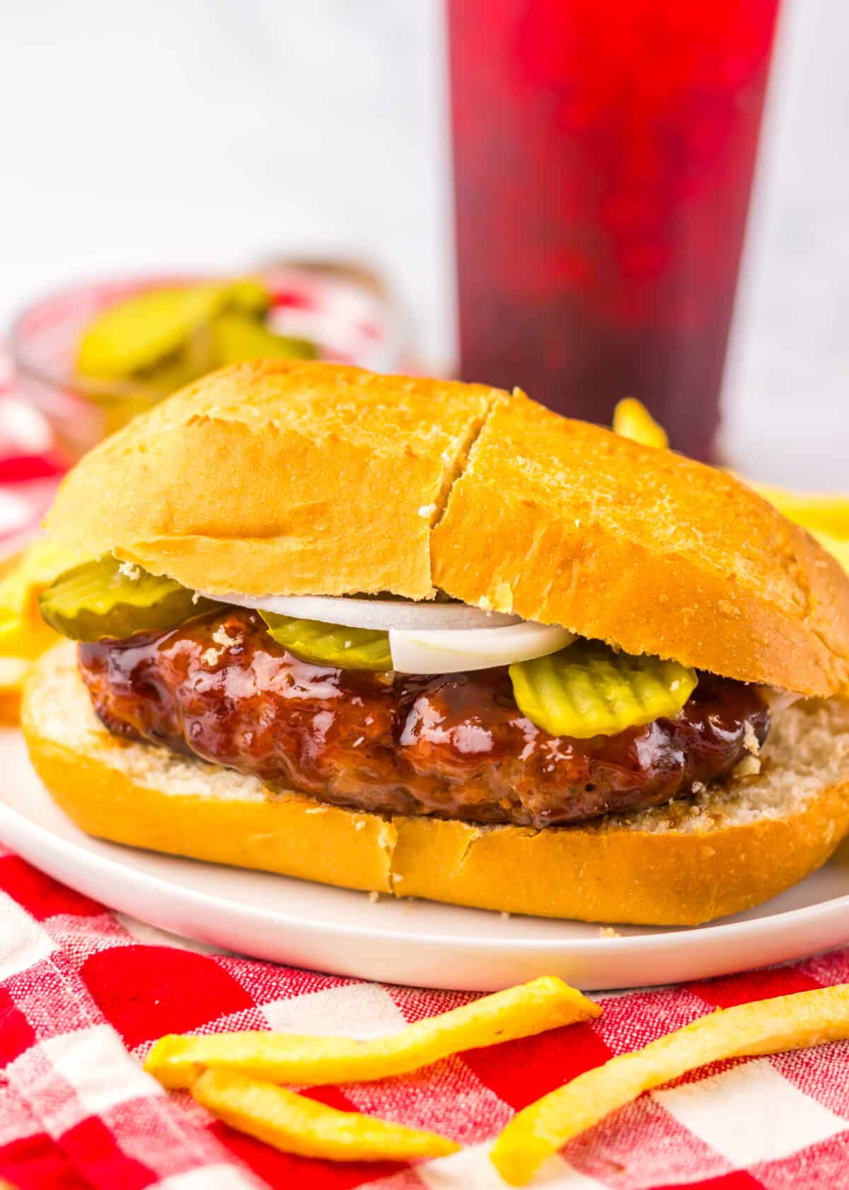 Copycat McRib sandwich topped with onions and pickles, served with fries on a rustic plate and red and white napkin.