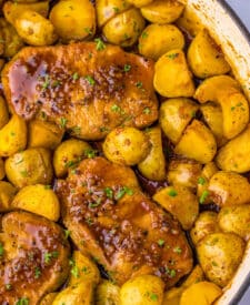 Fully cooked pork chops and baby potatoes coated in honey garlic sauce, garnished with parsley in a skillet.