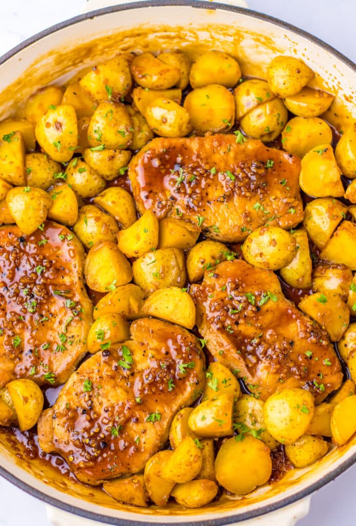 Close-up of glazed pork chops and halved baby potatoes in a skillet, covered in sticky garlic honey sauce.