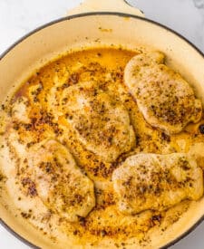 Seasoned pork chops searing in a large cream-colored skillet, developing a golden crust.