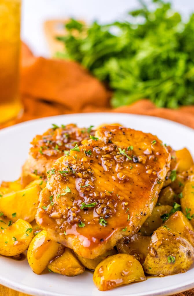 Sticky honey garlic pork chops served with baby potatoes on a plate, coated in a glossy glaze.