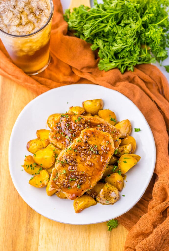 Sticky honey garlic pork chops served with baby potatoes on a plate, coated in a glossy glaze.