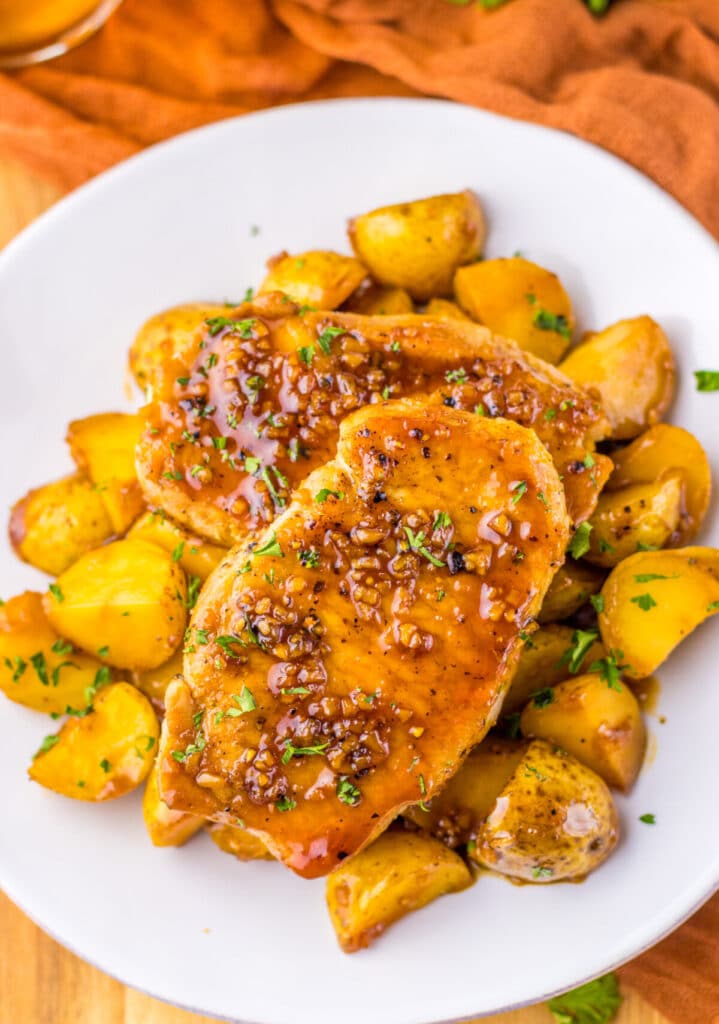Boneless pork chops in a sweet and savory garlic sauce with golden baby potatoes on a white plate.