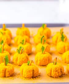 Mini pumpkin cheeseballs arranged neatly on a parchment-lined tray.
