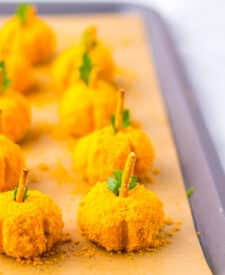 Mini pumpkin cheeseballs arranged neatly on a parchment-lined tray.