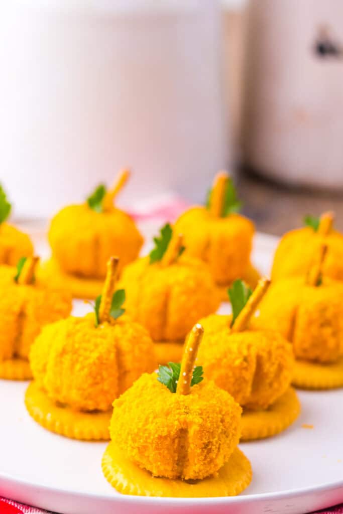 Pumpkin-shaped cheeseballs with pretzel stems arranged on a tray.
