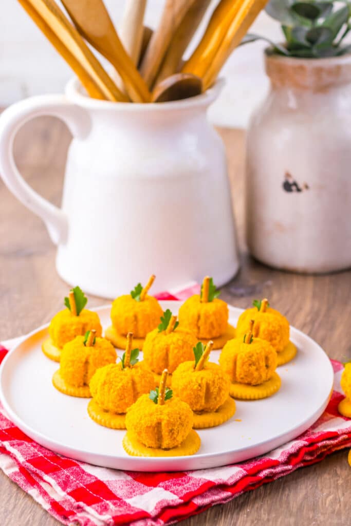 Pumpkin-shaped cheeseballs with pretzel stems arranged on a tray.