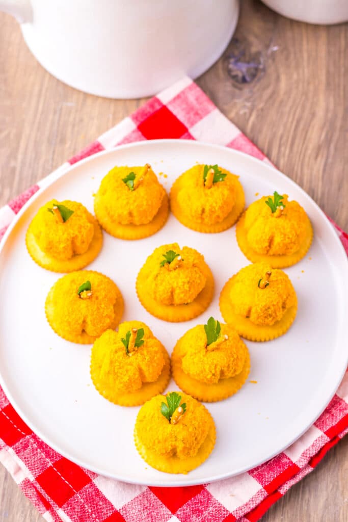 Pumpkin-shaped cheeseballs with pretzel stems arranged on a tray.