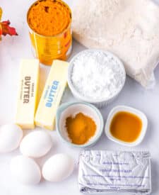 Ingredients for pumpkin gooey butter bars including butter, cake mix, pumpkin puree, cream cheese, eggs, and powdered sugar.