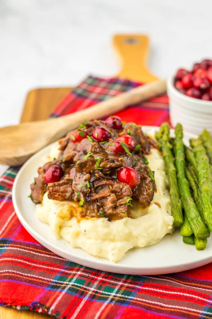 Slow Cooker Cranberry Roast Beef on top of fluffy mashed potatoes with asparagus