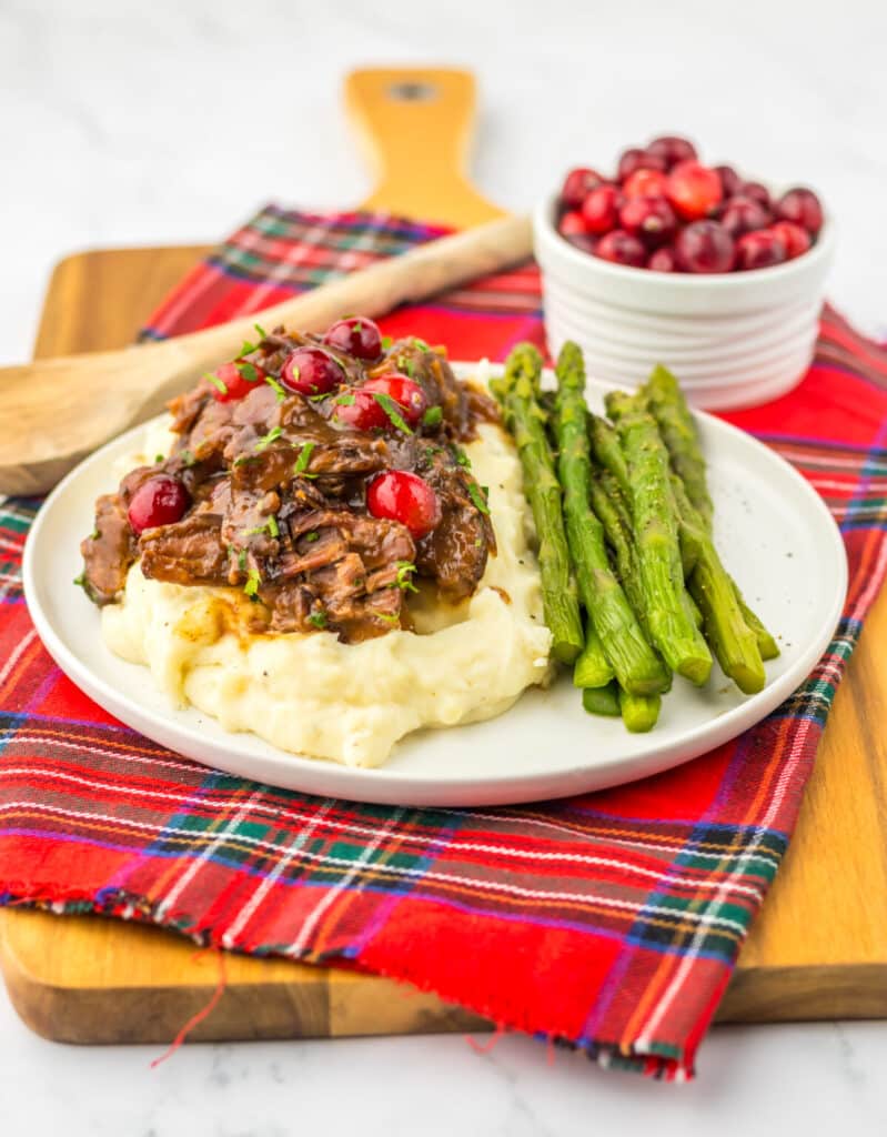 Slow Cooker Cranberry Roast Beef on top of fluffy mashed potatoes with asparagus