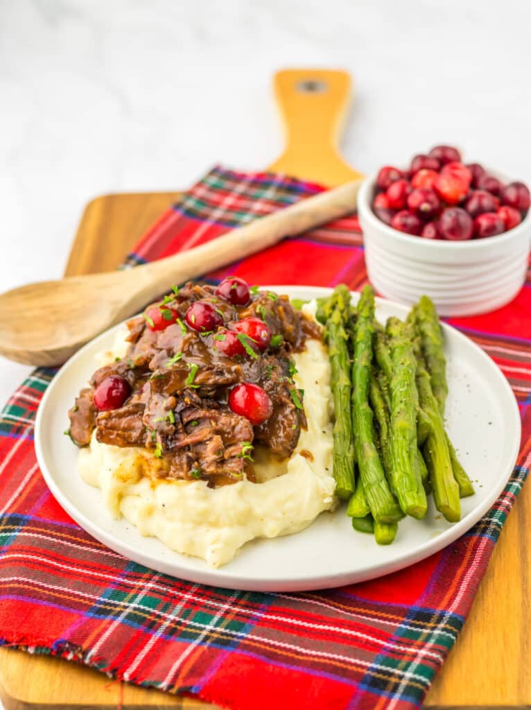 Slow Cooker Cranberry Roast Beef on top of fluffy mashed potatoes with asparagus