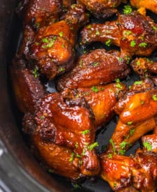 Close-up of glazed honey garlic wings topped with sesame seeds and fresh herbs.