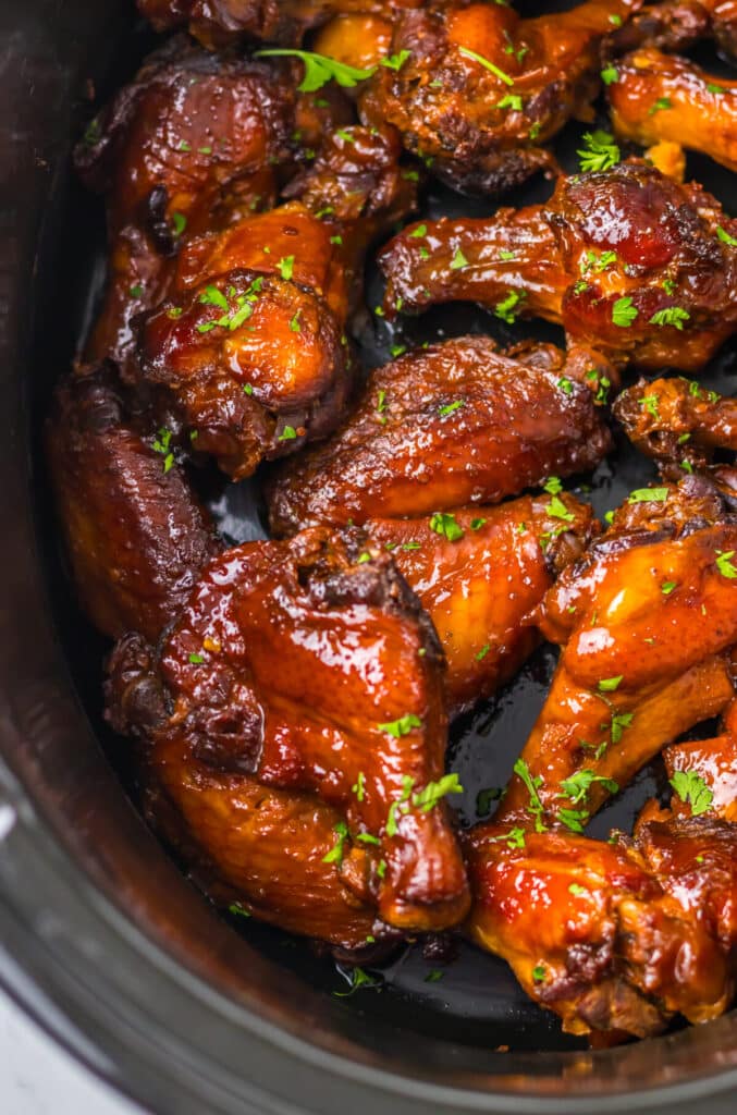 Close-up of glazed honey garlic wings topped with sesame seeds and fresh herbs.