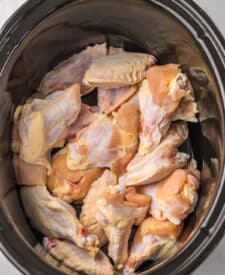 Raw chicken wings placed in a slow cooker with sauce ingredients.