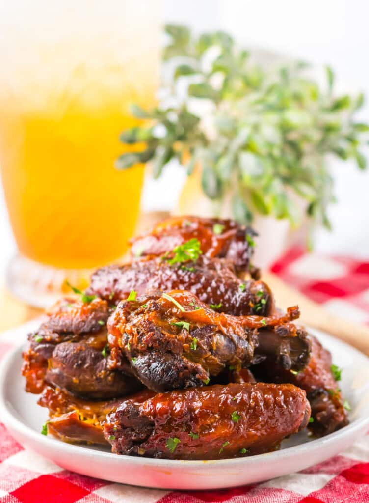 Honey garlic chicken wings in a white bowl with parsley garnish and iced tea glasses.