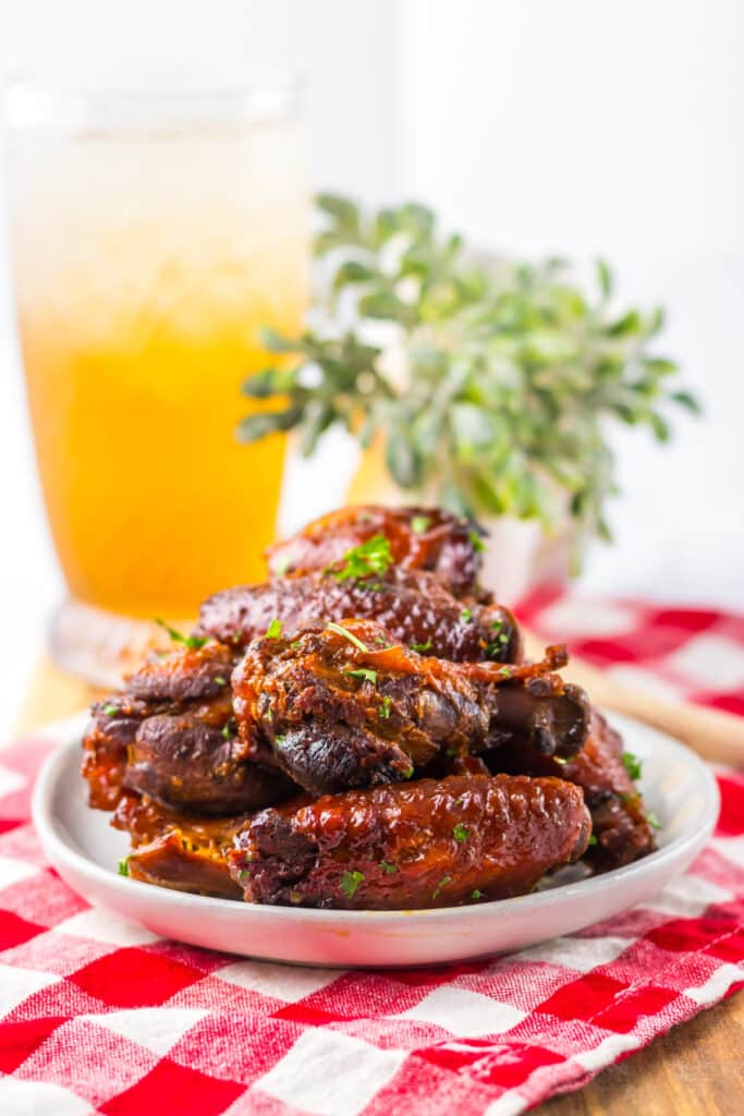 Honey garlic chicken wings in a white bowl with parsley garnish and iced tea glasses.