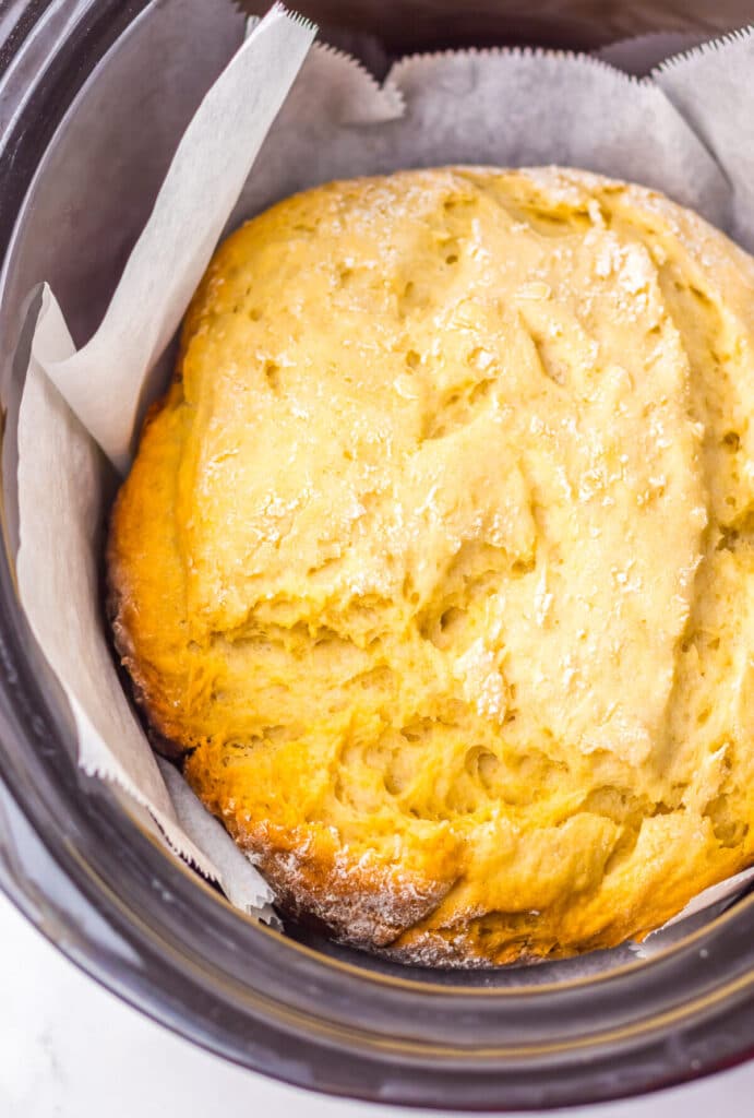 Golden brown slow cooker mock sourdough bread in parchment inside the pot.