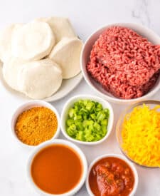 Ingredients for taco bubble up bake including ground beef, cheese, biscuits, salsa, and seasonings.