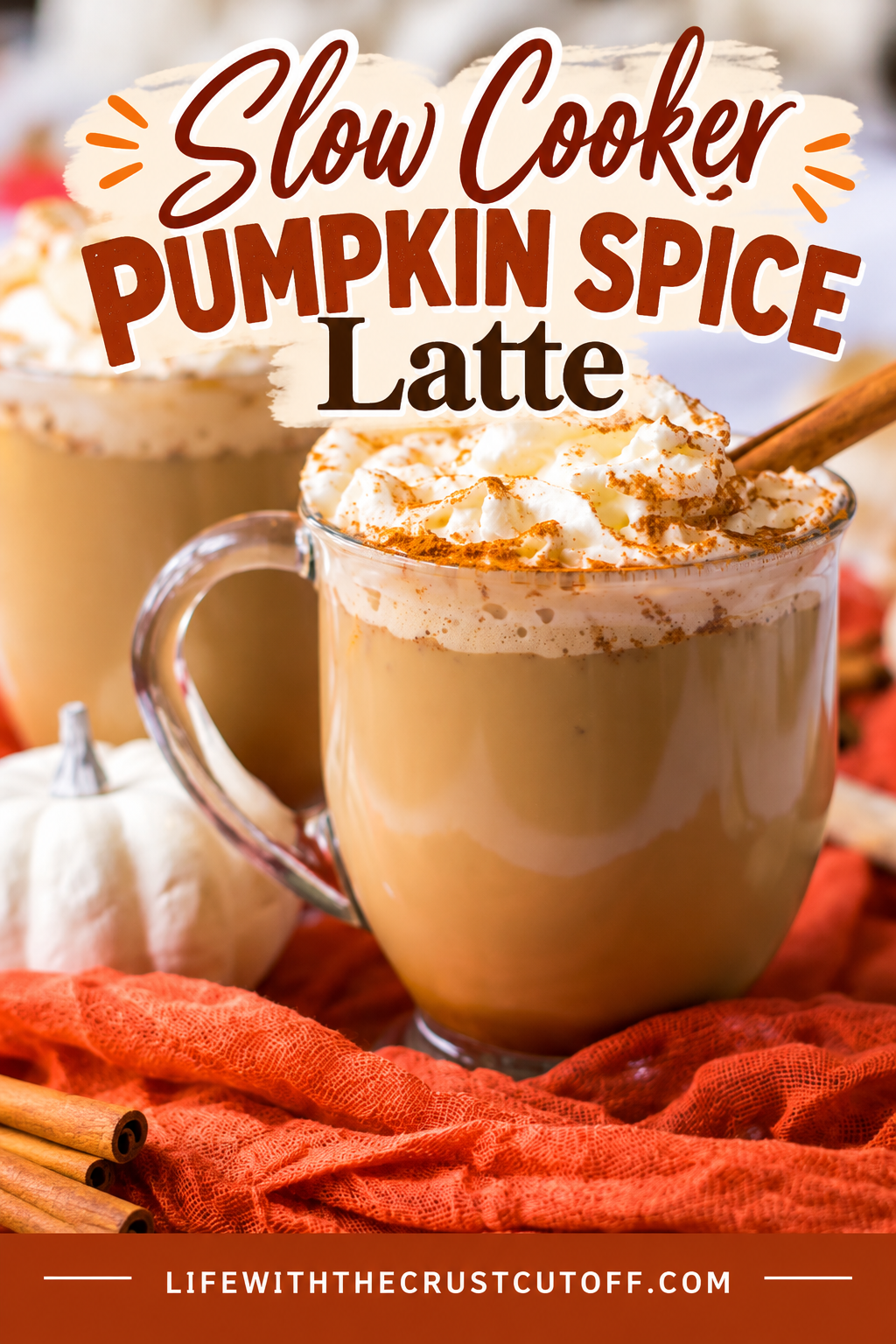 Slow Cooker Pumpkin Spice Latte topped with whipped cream and cinnamon and served with cinnamon sticks and a small white pumpkin.