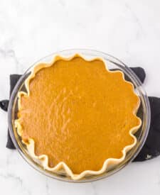 Pouring the creamy apple butter filling into a par-baked pie crust on a white surface.