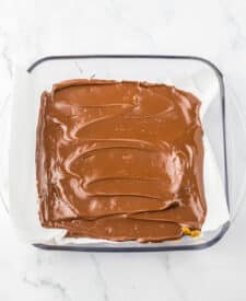 Homemade English toffee slab with melted chocolate layer spread over buttery caramel toffee base on parchment paper.