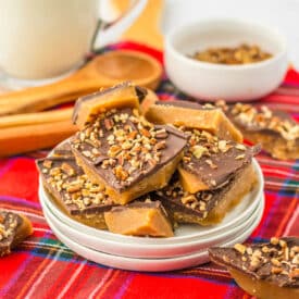 Pieces of English toffee broken into squares topped with chocolate and chopped almonds on red plaid cloth
