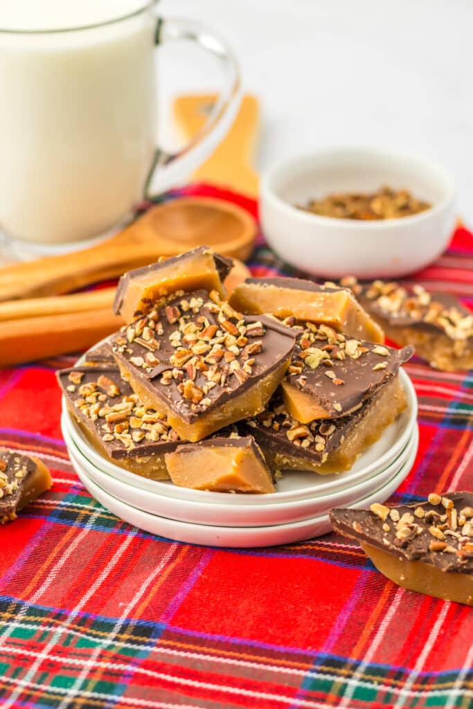 Pieces of English toffee broken into squares topped with chocolate and chopped almonds on red plaid cloth