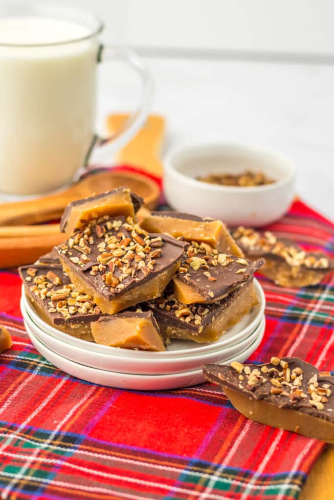Pieces of English toffee broken into squares topped with chocolate and chopped almonds on red plaid cloth
