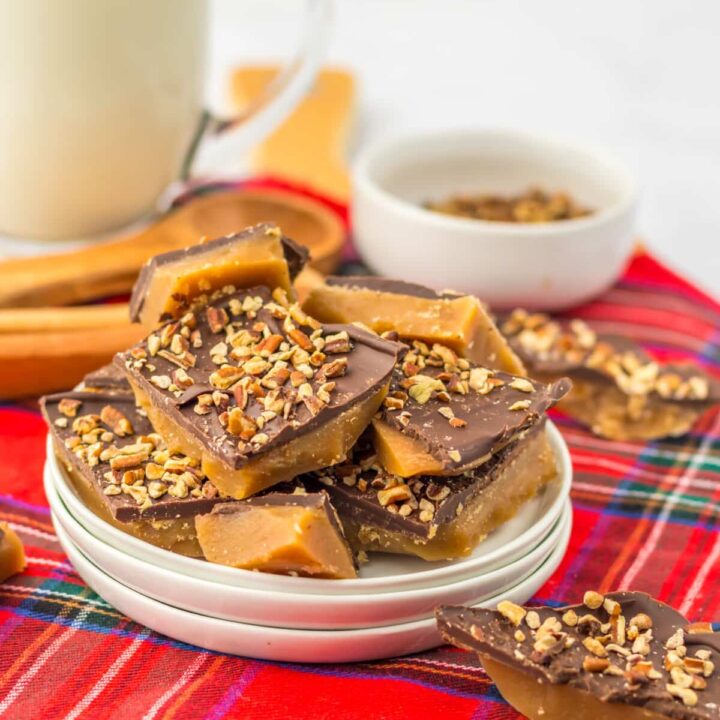 Pieces of English toffee broken into squares topped with chocolate and chopped almonds on red plaid cloth