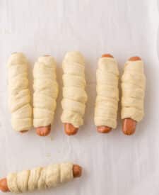 Pretzel dogs after boiling, lined up on a baking sheet before baking.