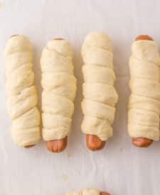 Pretzel dogs after boiling, lined up on a baking sheet before baking.