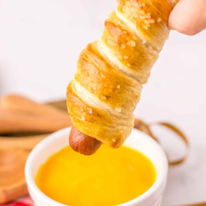 Golden brown pretzel dogs on a white plate with red plaid napkin.