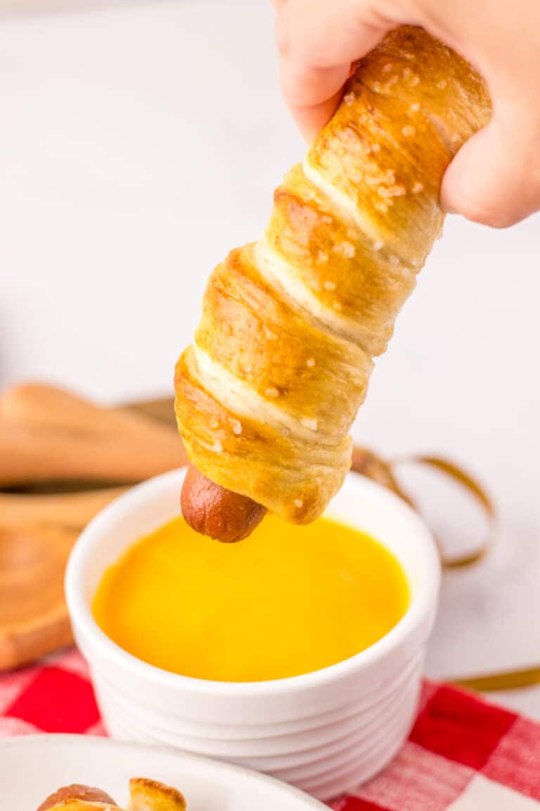 Golden brown pretzel dogs on a white plate with red plaid napkin.