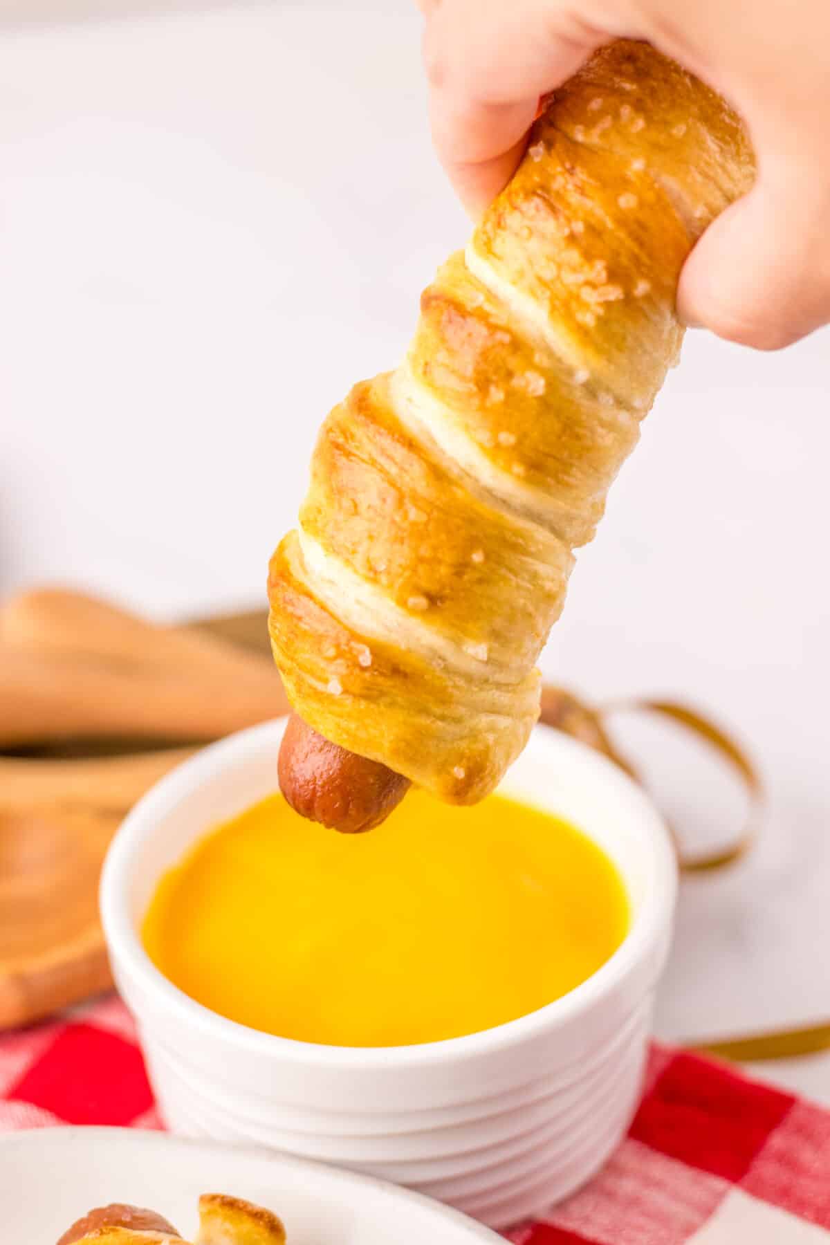 Golden brown pretzel dogs on a white plate with red plaid napkin.
