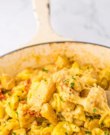 Spoon lifting cheesy chicken tortellini from skillet showing creamy sauce