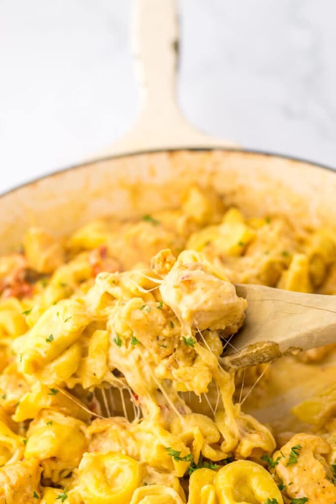 Spoon lifting cheesy chicken tortellini from skillet showing creamy sauce