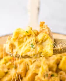 Spoon lifting cheesy chicken tortellini from skillet showing creamy sauce