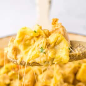Spoon lifting cheesy chicken tortellini from skillet showing creamy sauce