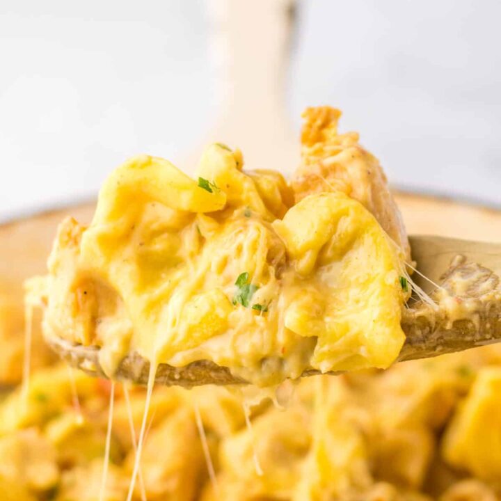 Spoon lifting cheesy chicken tortellini from skillet showing creamy sauce