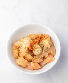 Seasoned uncooked chicken in a white bowl ready to cook for Marry Me Chicken Tortellini.