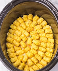 Adding a layer of frozen tater tots over the creamy chicken mixture in the slow cooker.